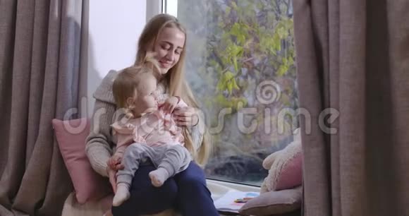 年轻漂亮的白人母女坐在窗台上透过窗户向外看妇女视频的预览图