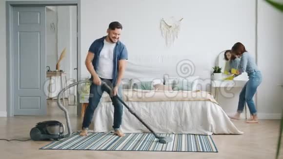 男人和女人在家里打扫卫生时玩得很开心吸尘和跳舞视频的预览图