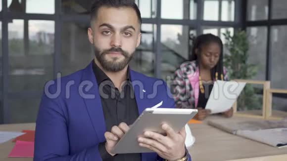 白人男子看着他的平板电脑在前景微笑非洲裔美国妇女在检查图纸视频的预览图