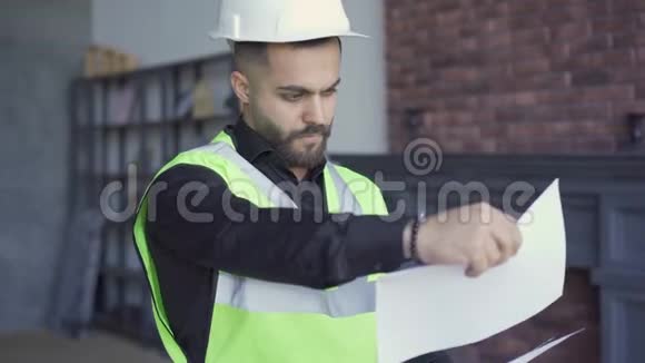 建筑工人在头盔和绿色夹克审查图纸专业的工作看报纸的人视频的预览图
