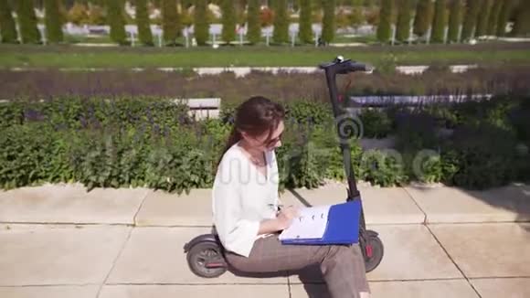 女工人用笔记本开发技术在夏日阳光明媚的一个美丽的公园里坐在电动滑板车上视频的预览图