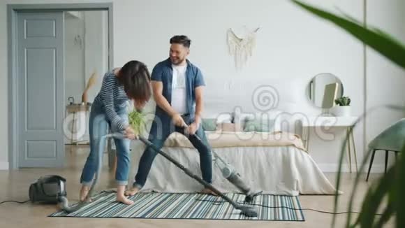 女孩和男人在卧室里用吸尘器吸地毯在打扫卫生时笑着玩视频的预览图