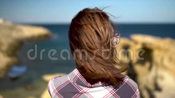 一个年轻的女人站在大海的背景上那个女孩的头发在风中摇动一个女人和她站在一起视频的预览图