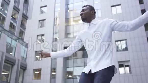 在城市街道上的现代商务中心前跳舞的美国黑人男子穿着白色衬衫视频的预览图