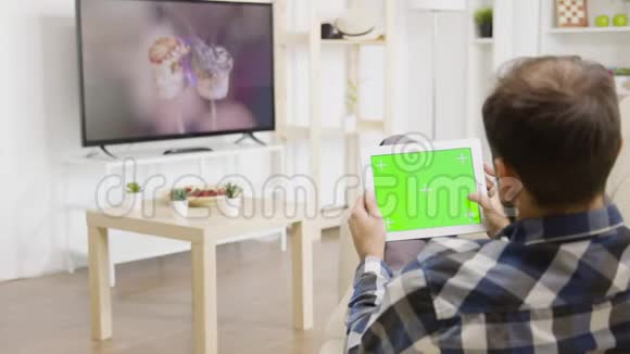 男人一边看电视一边摸着绿色屏幕数字平板电脑视频的预览图