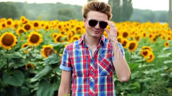 酷又时尚的年轻男性农民摘下太阳镜成功地站在向日葵的背景上视频的预览图