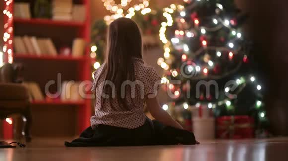 晚上一个小女孩坐在房间的地板上欣赏圣诞树视频的预览图
