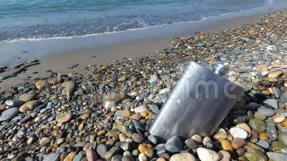 海滩上鹅卵石上的老式金属臀部烧瓶庆祝男人海上度假视频的预览图