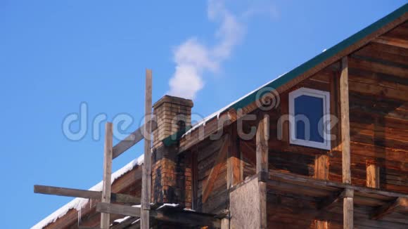 冬天在蓝天的映衬下木屋屋顶上的砖石烟囱冒出浓烟视频的预览图