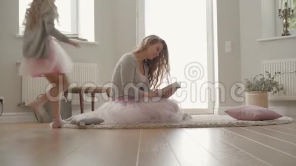 漂亮的白种人女人穿着红裙子和灰色衬衫坐在地毯上看书可爱的小女孩视频的预览图