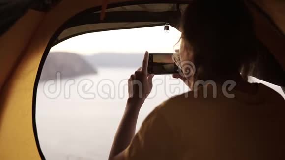 年轻女孩独自露营女孩正在从她的智能手机上拍照从帐篷外面看到美丽的景色大海视频的预览图