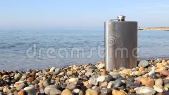 海滩上鹅卵石上的老式金属臀部烧瓶视频的预览图