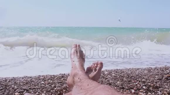 一个躺在海边的人的腿蓝色海洋背景上的男性腿一个男人喜欢在鹅卵石海滩度假视频的预览图