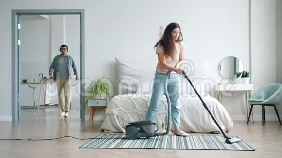 家庭主妇用吸尘器打扫地板而戴耳机的男人则在卧室里跳舞视频的预览图