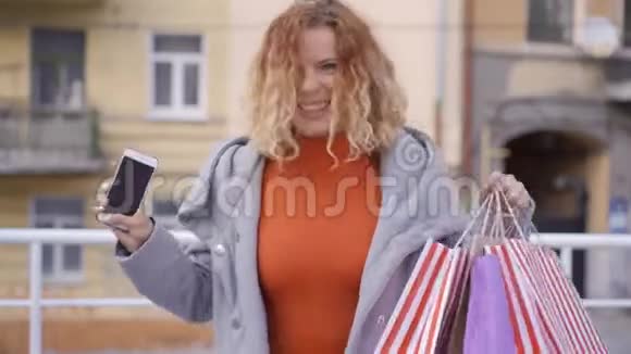 兴奋的红发女孩手里拿着购物袋和手机在空中行走成年妇女对她满意视频的预览图