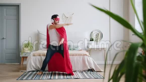 戴着超级英雄服装戴着红斗篷戴着面具在家跳舞的戴着耳机的家伙视频的预览图