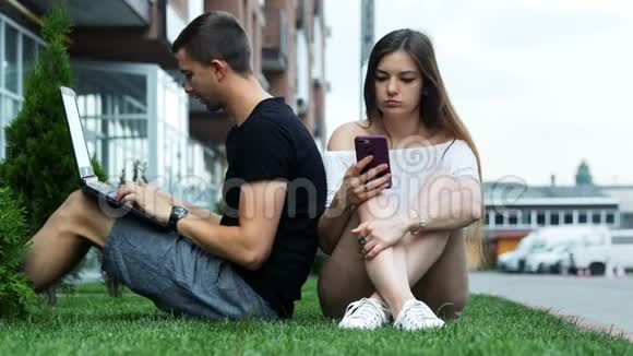 朋友们在公园里放松男人用笔记本电脑女孩喜欢智能手机视频的预览图