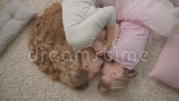 幸福的白种人母亲和她穿着红色裙子的小女儿躺在家里蓬松的地毯上妇女和女孩视频的预览图