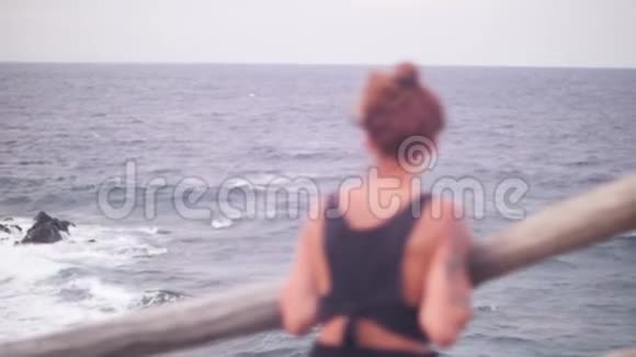 一个红头发的女人在刮风的日子里看着大海的景色视频的预览图