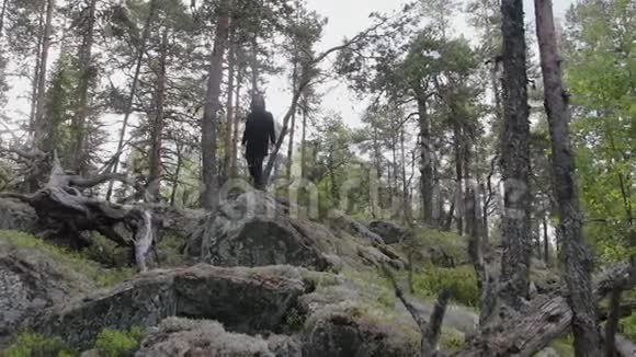 穿着黑色羊毛衫和太阳镜的人从森林里的岩石悬崖上跳下视频的预览图