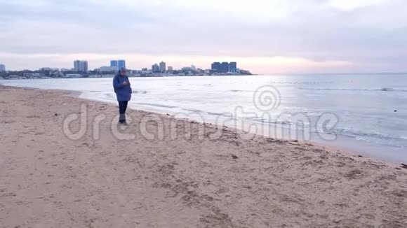 曼特维尔走在海边沙滩上手里拿着电话靠近沿海城镇视频的预览图