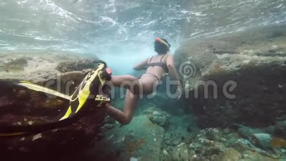 一个性感的年轻女人带着鳍在巨大的岩石附近水下游泳视频的预览图