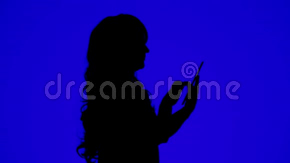 一个身材苗条卷发的女人在蓝色背景的平板电脑上用信使传达信息的剪影视频的预览图