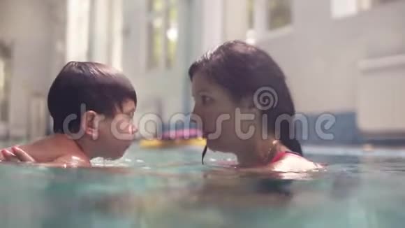 一个浓黑的女人教她的孩子潜入水中在游泳池里游泳妈妈和儿子游泳视频的预览图