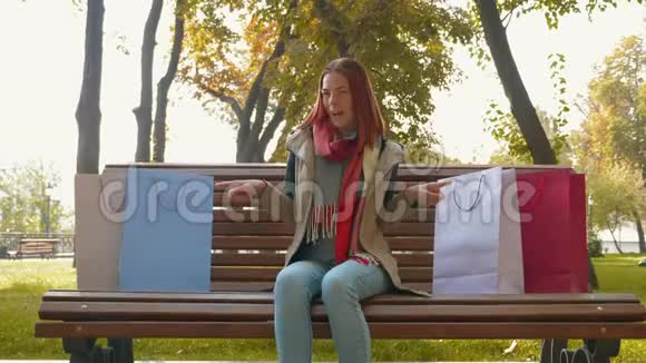 一个长着狐臭头发的女孩坐在公园的长凳上指出她买的纸袋视频的预览图