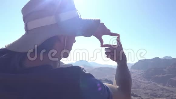在阳光明媚的日子里戴着帽子的年轻人用双手在山顶上令人惊叹的风景视频的预览图