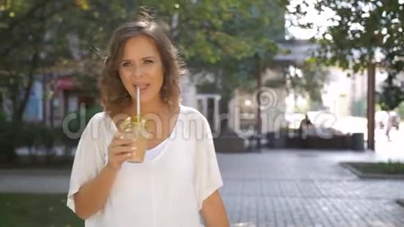 快乐的中年妇女在炎热的夏天喝着一杯冷拿铁走在街上视频的预览图