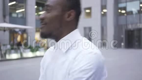 穿着白色衬衫的开朗的非裔美国人在城市街道上的现代商务中心前跳舞视频的预览图