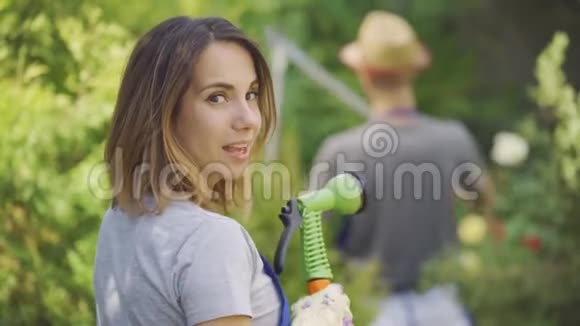 幸福的女人和一个男人正在花园里工作女孩从水管里溅到她丈夫身上快乐的家庭视频的预览图