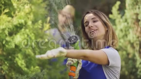 一幅可爱的白种人女人在前景中玩弄水管而男人在砍树叶时的肖像视频的预览图