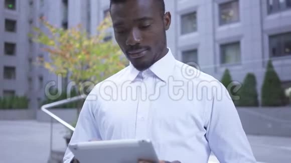 英俊的非裔美国人穿着白色衬衫站在城市街道上的平板电脑工作的肖像男性视频的预览图