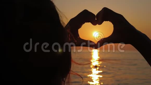 女孩在日落时的太阳背景上以心脏的形状牵手视频的预览图