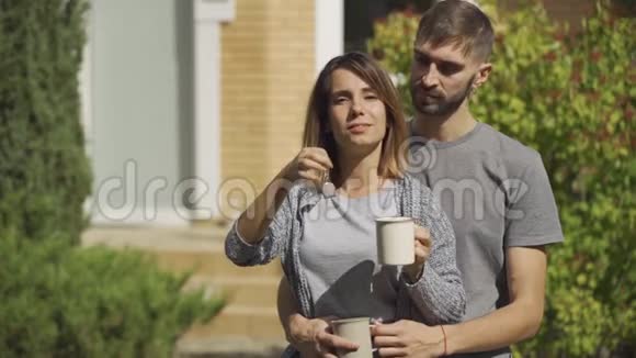 肖像欢乐白种人女人端着茶杯和帅哥站在大房子前少女秀场视频的预览图