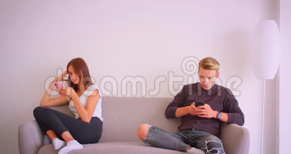 一对年轻貌美的情侣坐在沙发上用手机发短信的特写照片视频的预览图