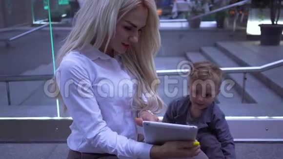 年轻漂亮的女商人在她的平板电脑上给小男孩展示了一些东西妈妈带着儿子去视频的预览图