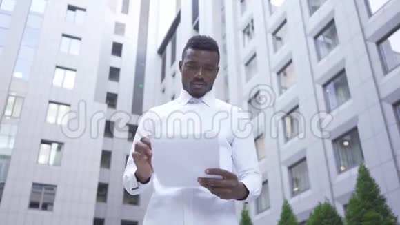 英俊的非裔美国人穿着白色衬衫在城市街道上处理文件男性商人或视频的预览图