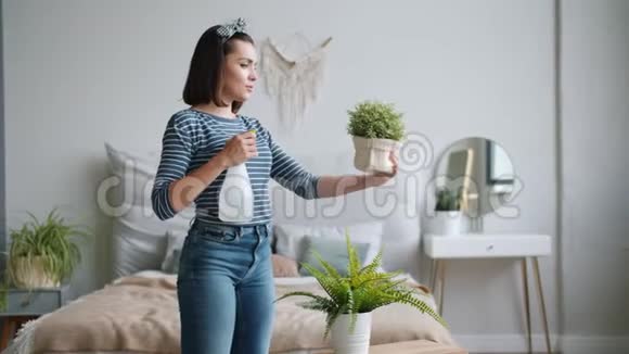 美丽的年轻女士在家里用喷壶向绿色植物泼水视频的预览图