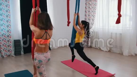 空中瑜伽两个女人进行训练一个腿在吊床上另一个靠在地上腿练习视频的预览图