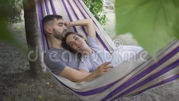 可爱的年轻白种人男女躺在花园的吊床上一起放松爱的情侣一起在户外视频的预览图