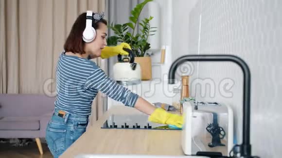 年轻女士清洁厨房和听耳机音乐的慢动作视频的预览图