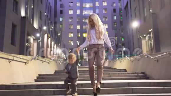 漂亮自信的女人穿着白色夹克她的小儿子走在城市街道的楼梯上免费儿童视频的预览图