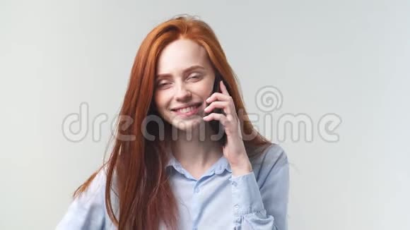 在Studio的白色背景下年轻红发女孩在智能手机上说话的肖像视频的预览图