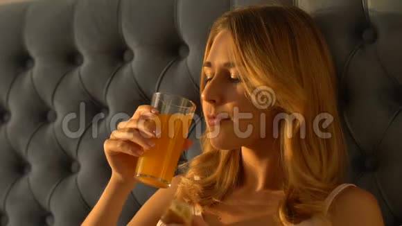 漂亮的女人坐在床上喝果汁吃羊角面包早餐视频的预览图