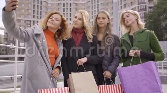 四个漂亮的女朋友在街上摆姿势其中一个在自拍四个时尚女人带着购物袋视频的预览图