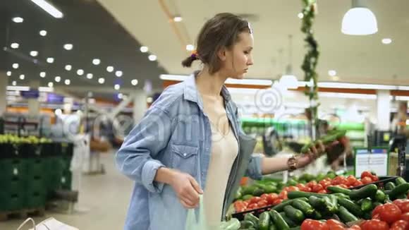 在超市购物在蔬菜系休闲的年轻女人挑选新鲜黄瓜把它们放进视频的预览图