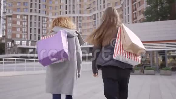 后景两个漂亮的女朋友走在街上带着购物袋说话和微笑免费生活方式视频的预览图